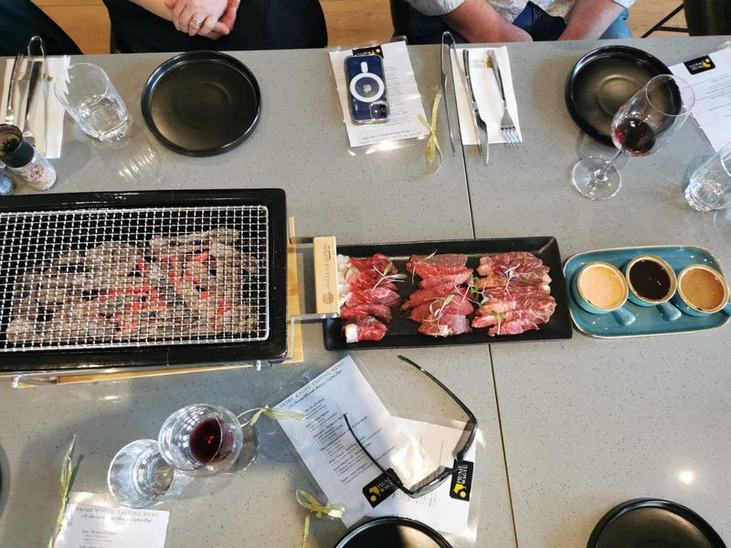 A tabletop grill with cuts of beef, sauces and glasses of wine